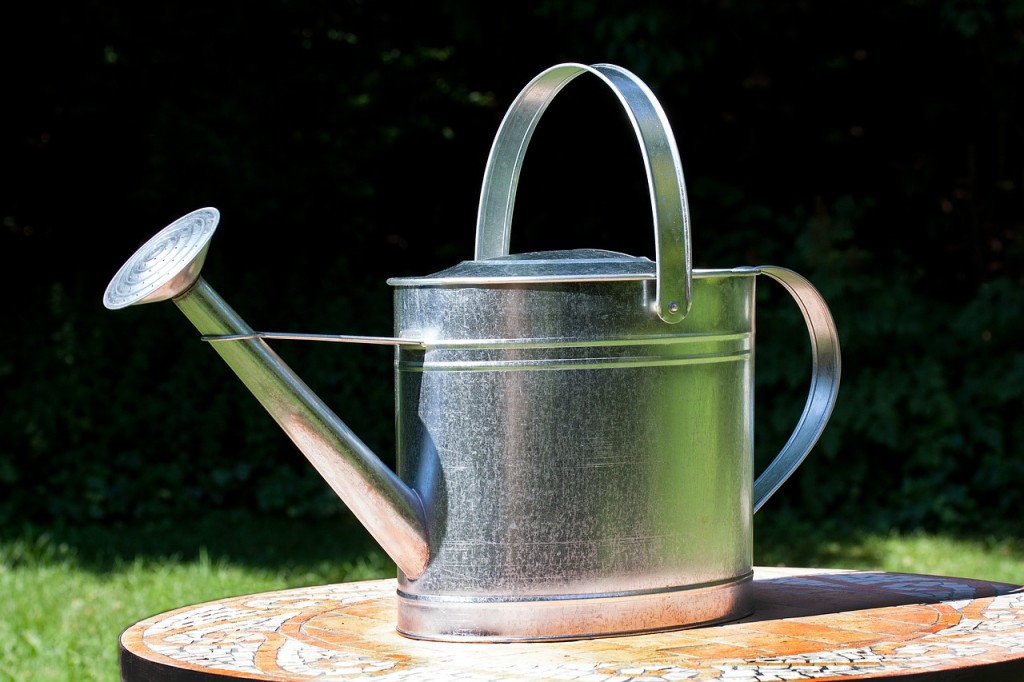 A metal watering can sitting on a patio table.