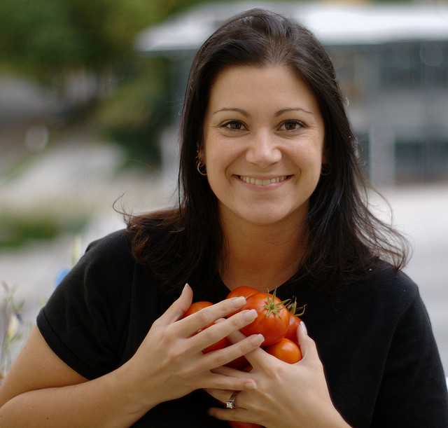 A woman holds several tomatoes to her chest, smiling.