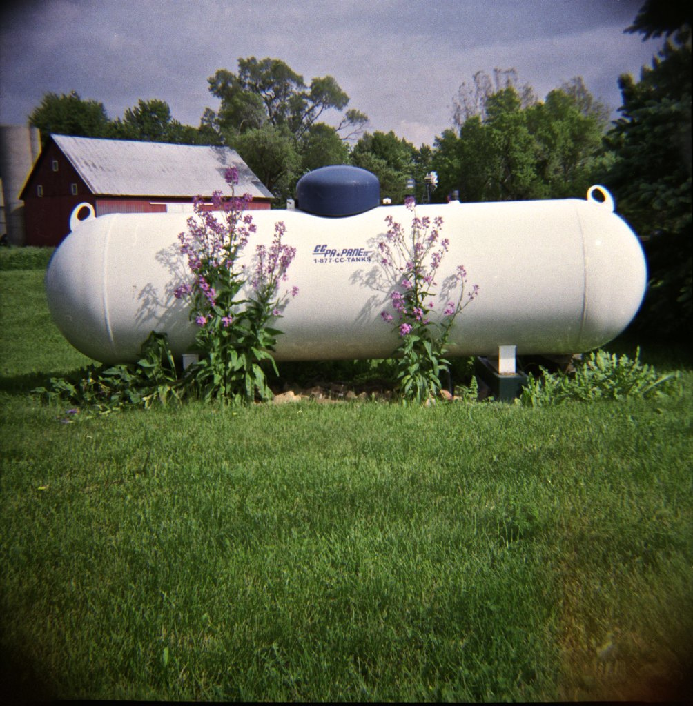 Propane is a fuel used to provide heat for some homes. Propane is stored in large tanks like that shown here. Source: “flowers and propane” by vistavision is licensed under the Creative Commons Attribution-NonCommercial-NoDerivs 2.0 Generic
