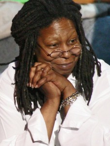 A woman with dreadlocks and a warm smile clasps her hands beside her face.