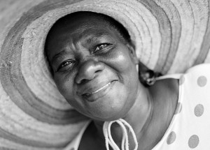 A smiling woman wears a polka-dotted blouse sun hat tied beneath her chin.