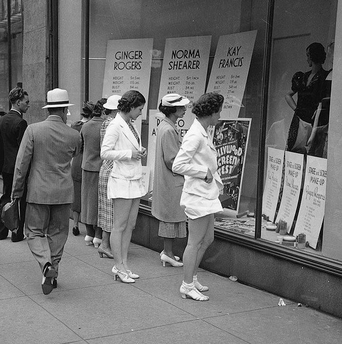 Women read the measurements of Ginger Rogers, Norma Shearer, and Kay Francis in store windows.