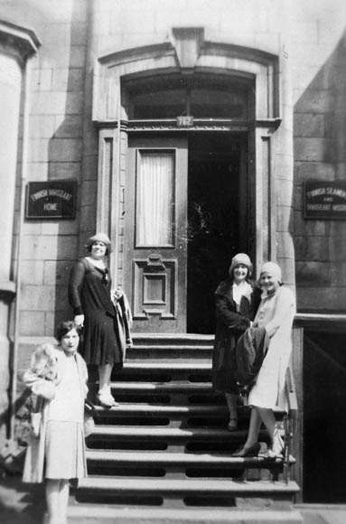 Four young women pose on the steps of a brownstone.