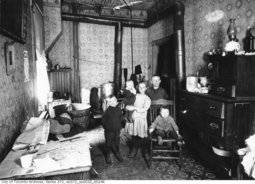 Five children pose in a room with a laundry line, a dresser, and a stove.