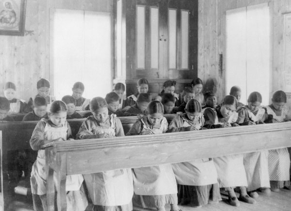 Girls and boys sit at long desks, heads bent over their schoolwork.