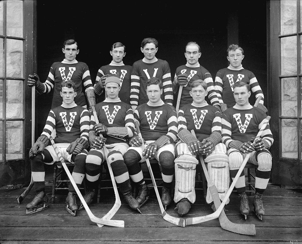 Ten men wearing hockey sweaters with a V and striped sleeves. They hold hockey sticks.