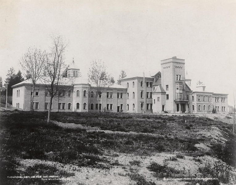 A stone building with multiple wings. The building is on a hill or at the edge of a cliff.