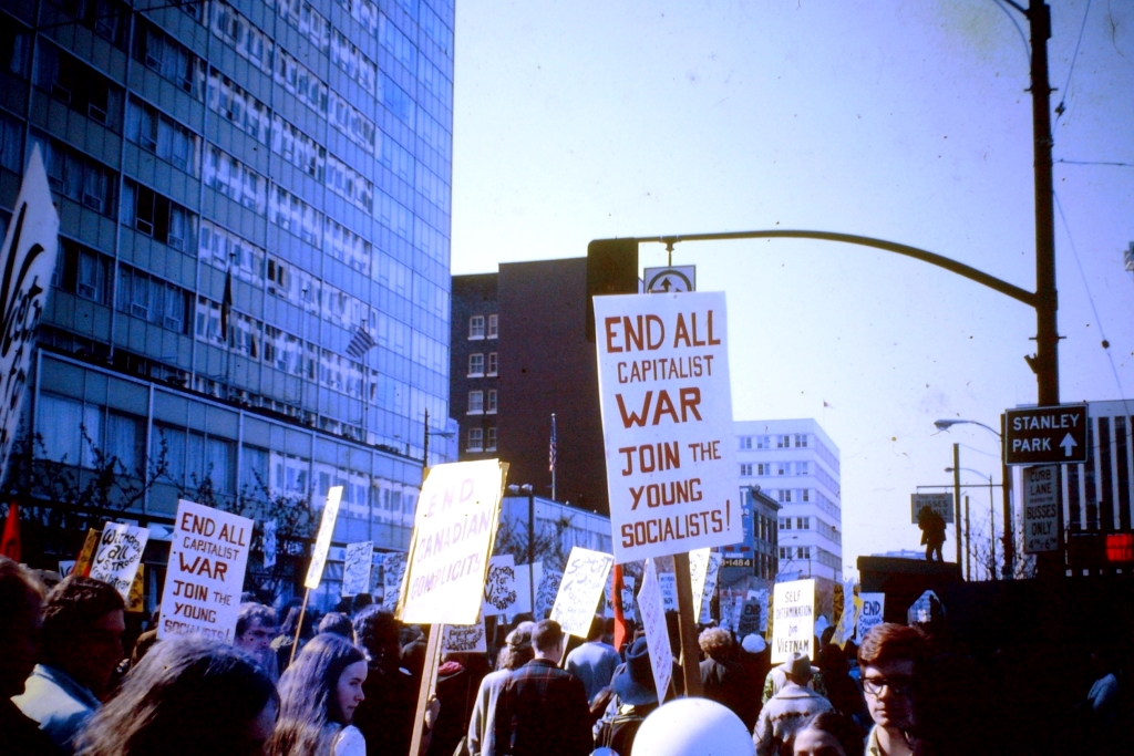 A protest march. Someone's sign says "End all capitalist war. Join the young socialists!"