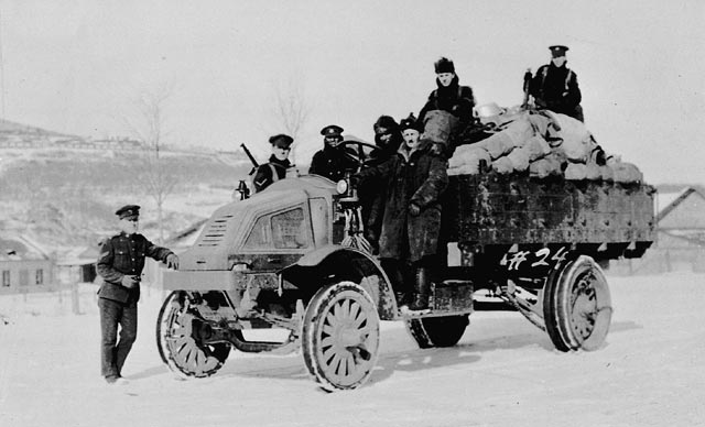 Seven men pose on top of and beside a military truck loaded with supplies.