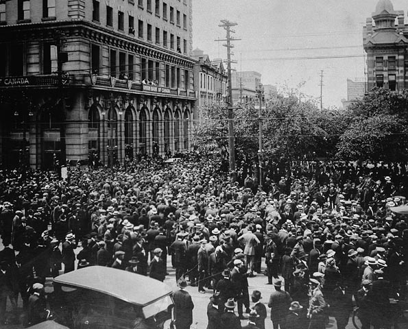 A city street packed with men. A car is in the foreground.