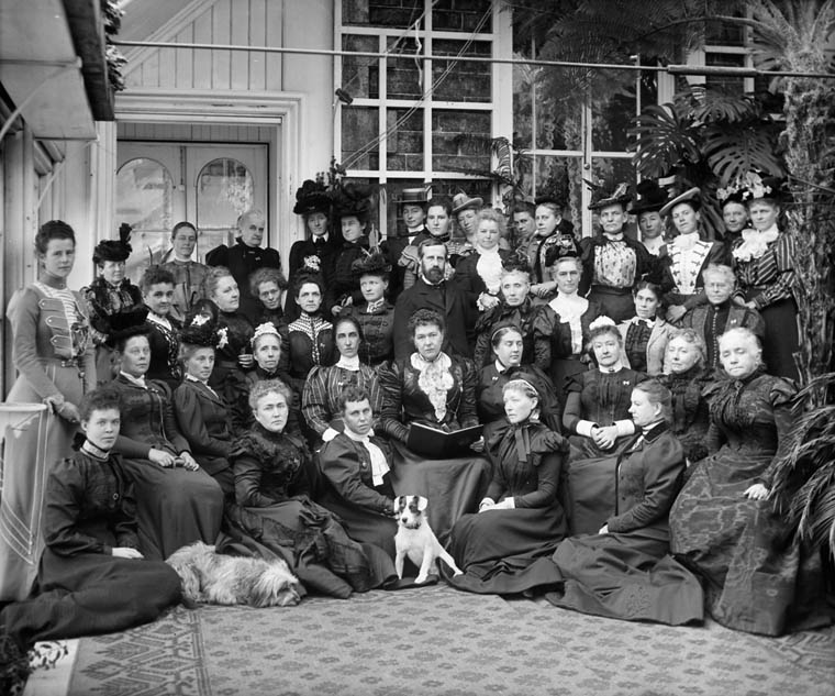 Forty women, one man, and two dogs pose for the camera, looking serious.