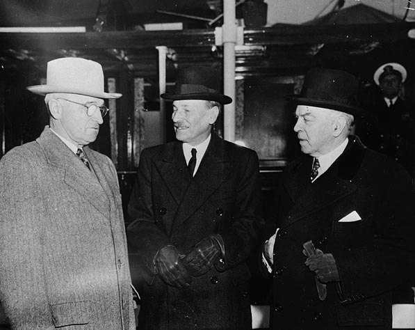 Three men in overcoats and formal hats stand on a ship&#039;s deck.