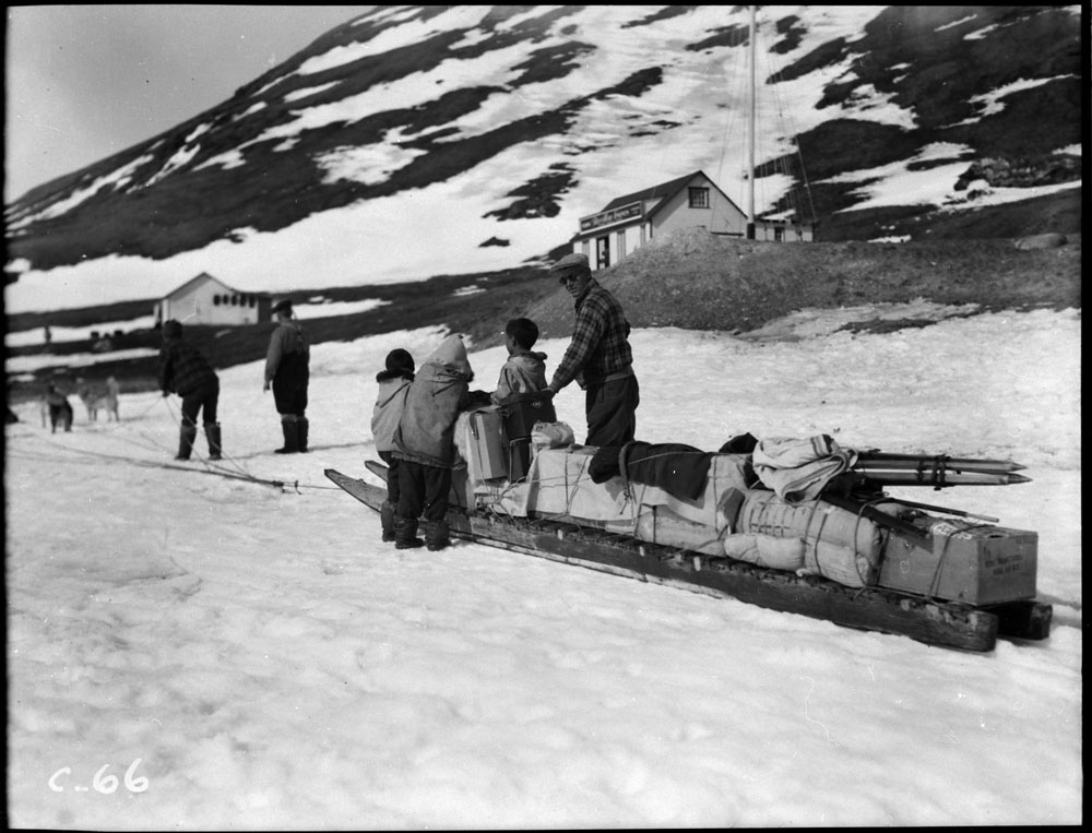 A man and three children stand around a long sled loaded with supplies.