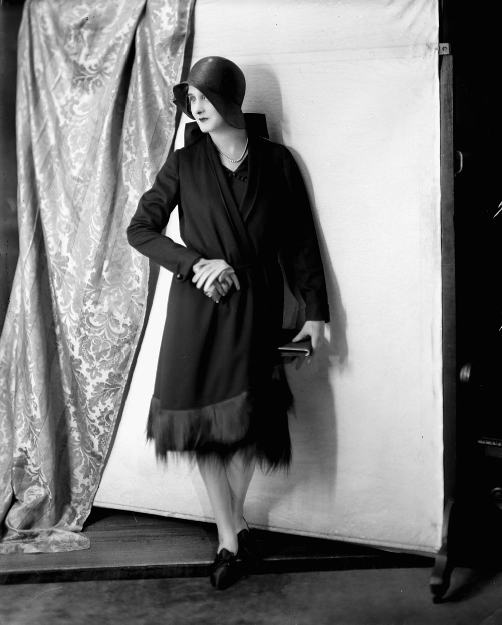 A model wears a knee-length dress and overcoat with a women's bowler hat.