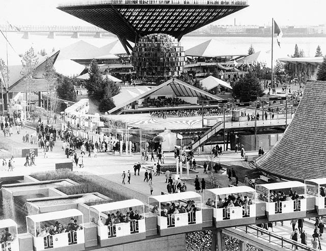 Display buildings with futuristic architecture. A monorail full of passengers is in the foreground.