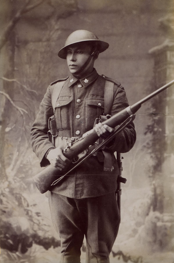A young man wearing a uniform with maple leaves on the lapels bears a rifle, looking serious.