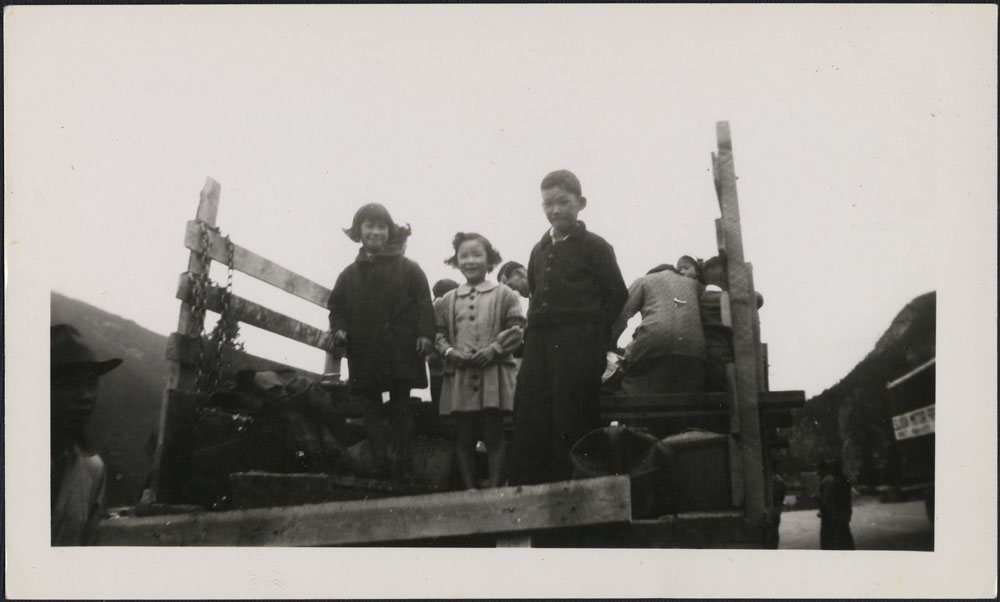 Two young girls and a boy stand in the back of a pick-up truck.
