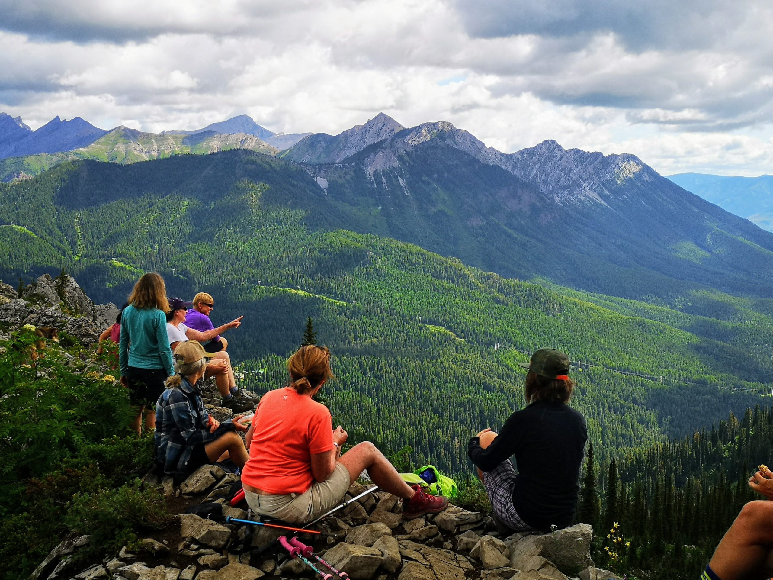 A group of people sit on the top of a moutain, looking out across a valley
