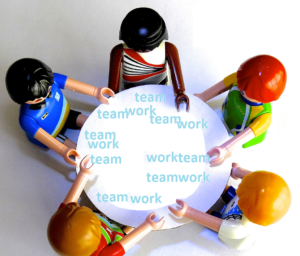 A group of lego people gathered around a toy table that has 'team work' written on it