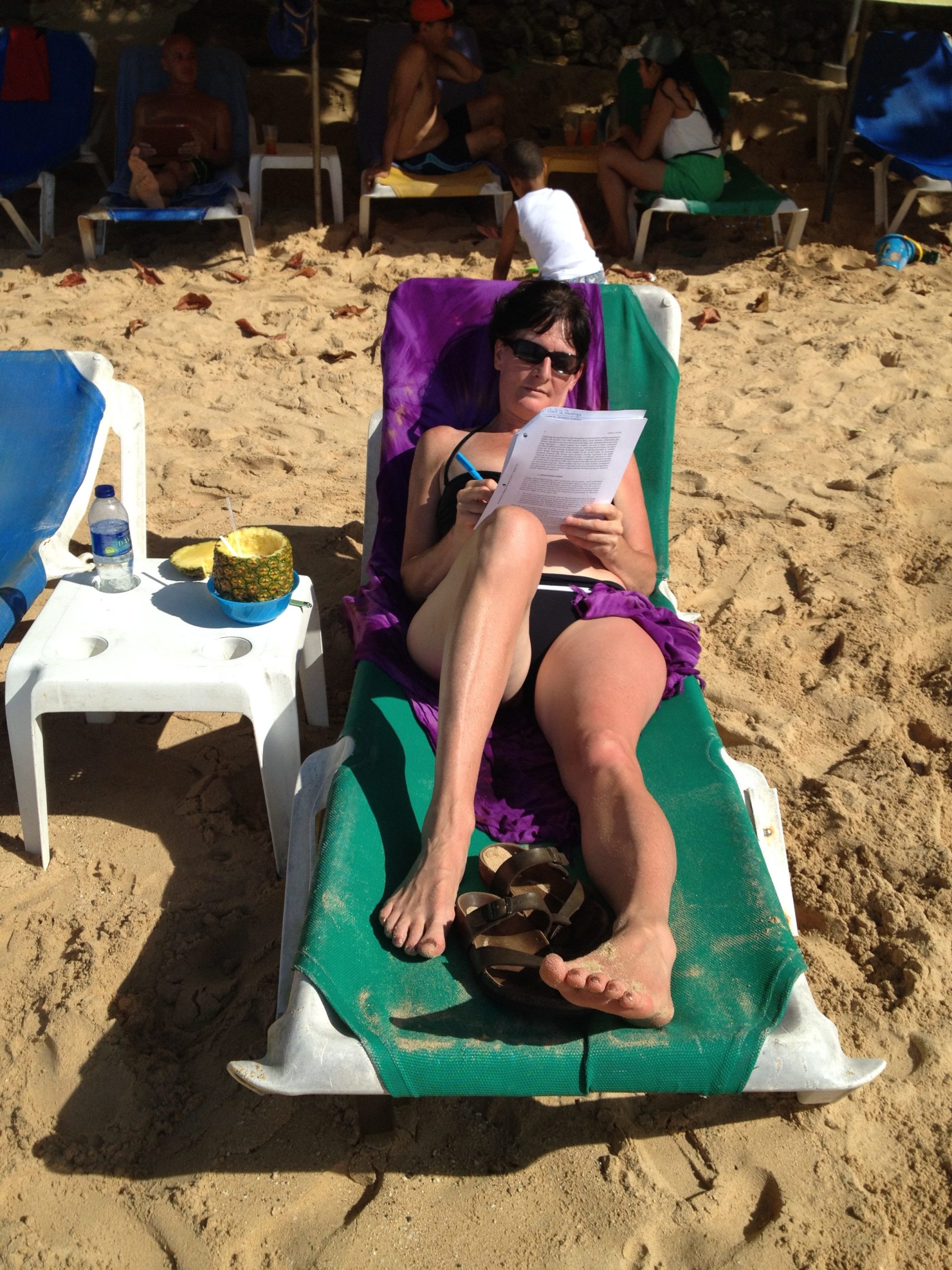 Mary Shier sitting in a lounge chair in her bathing suit on a beach taking notes