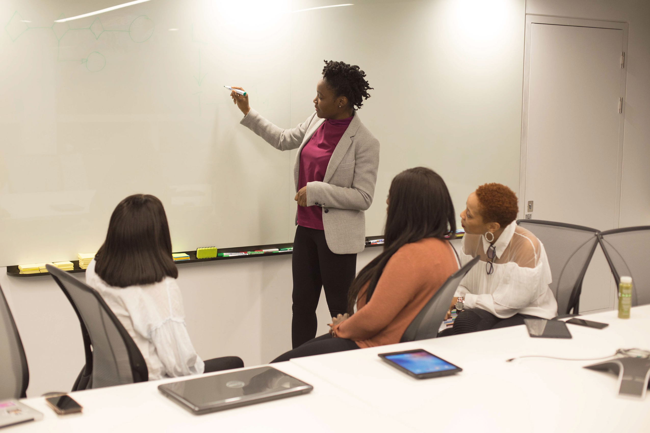 An instructor writes on a whiteboard while three students listen