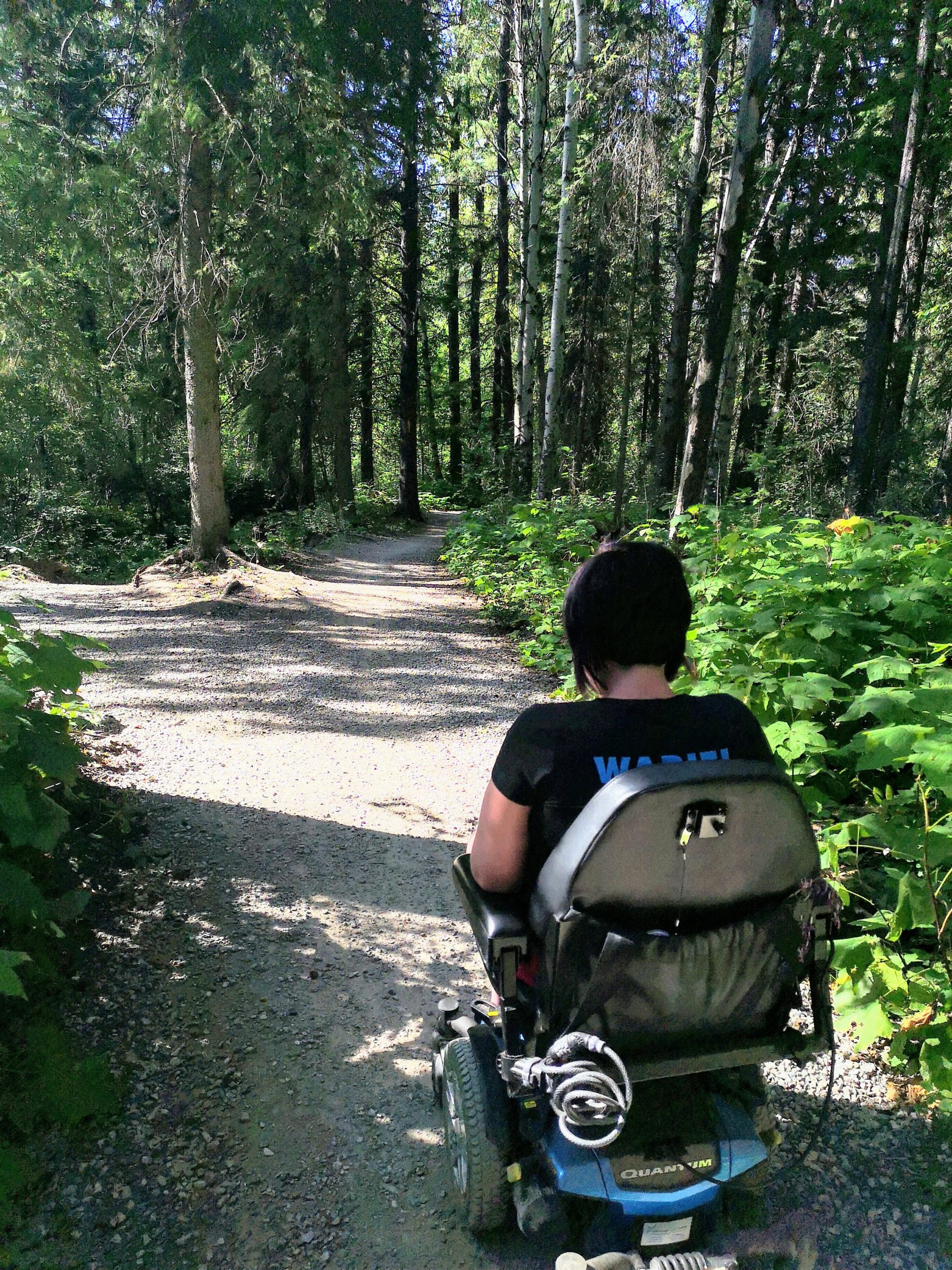 A woman navigates through a forest trail on a moterized chair