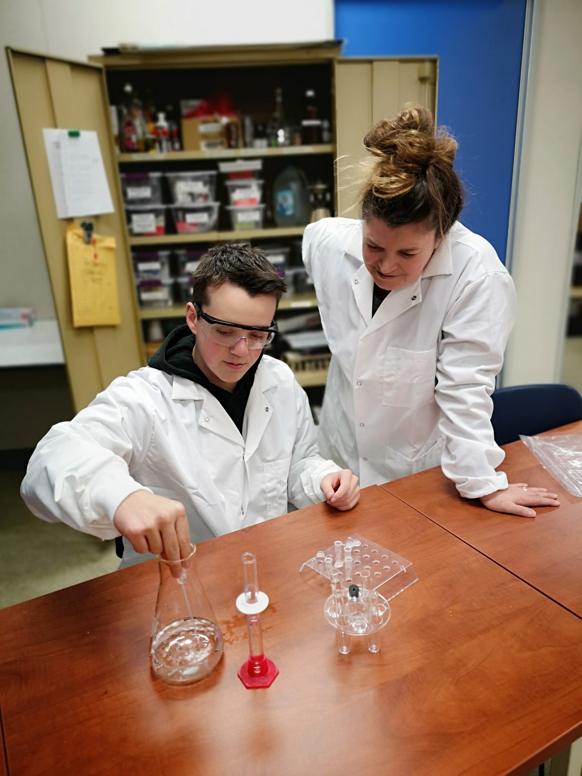 Two students measure chemicals into a beaker