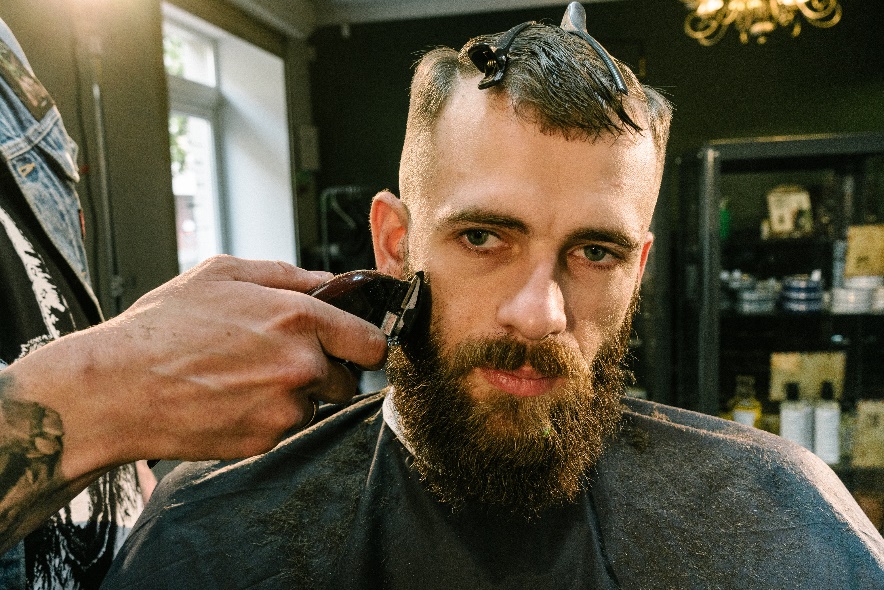 A clipper with a guard is being used to trim a client's beard.
