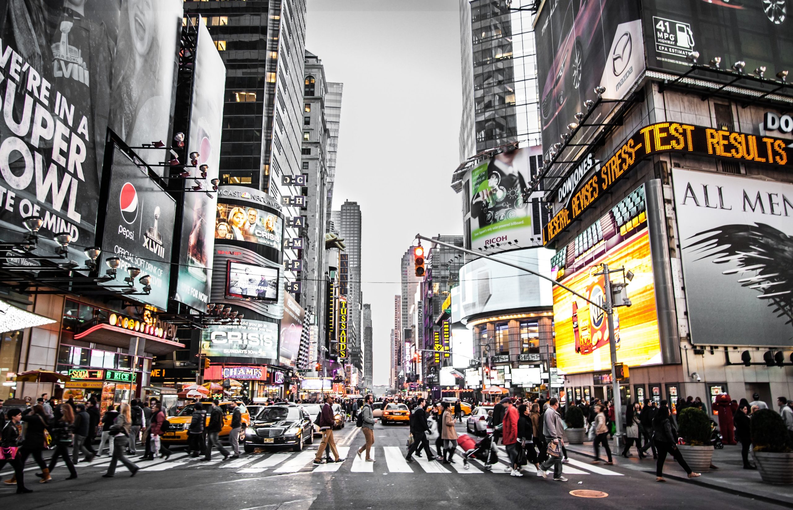 A busy urban crosswalk surrounded by high-rise buildings showcasing various retail advertisements and large buildboards.