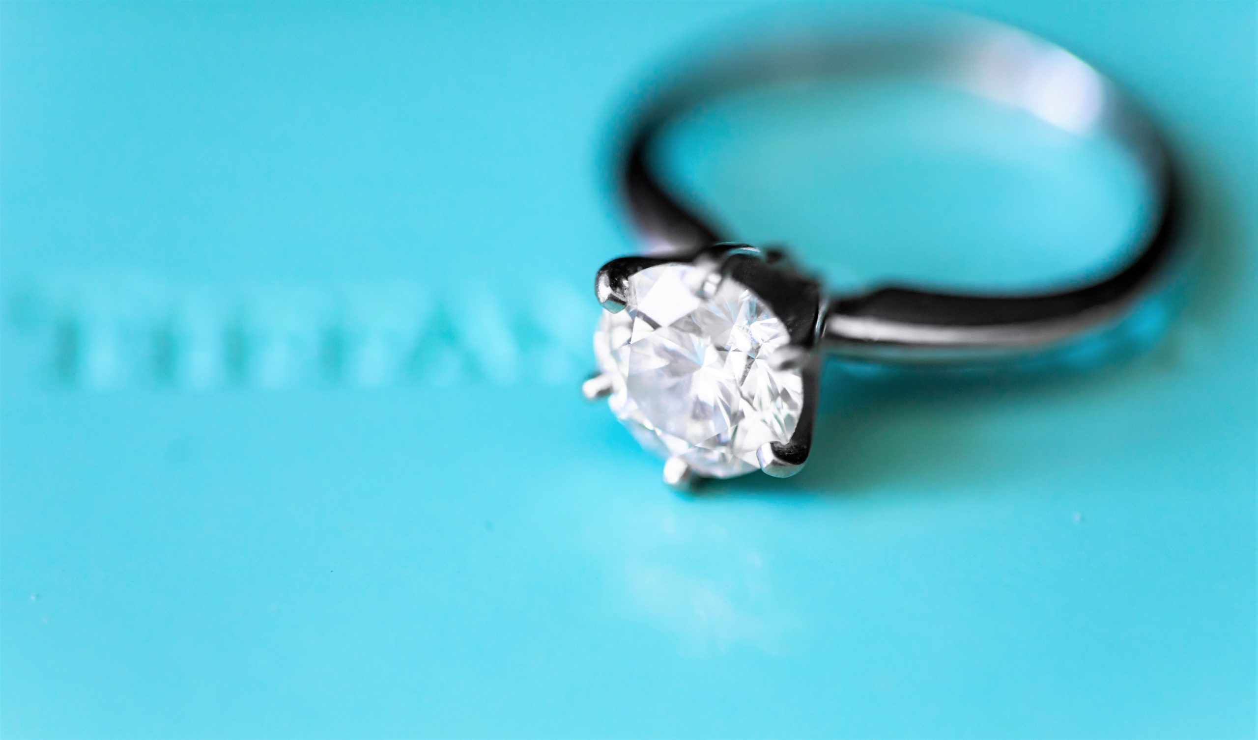 Photo of a diamond engagement ring against a robin's egg blue box that is presumably the brand, Tiffany's