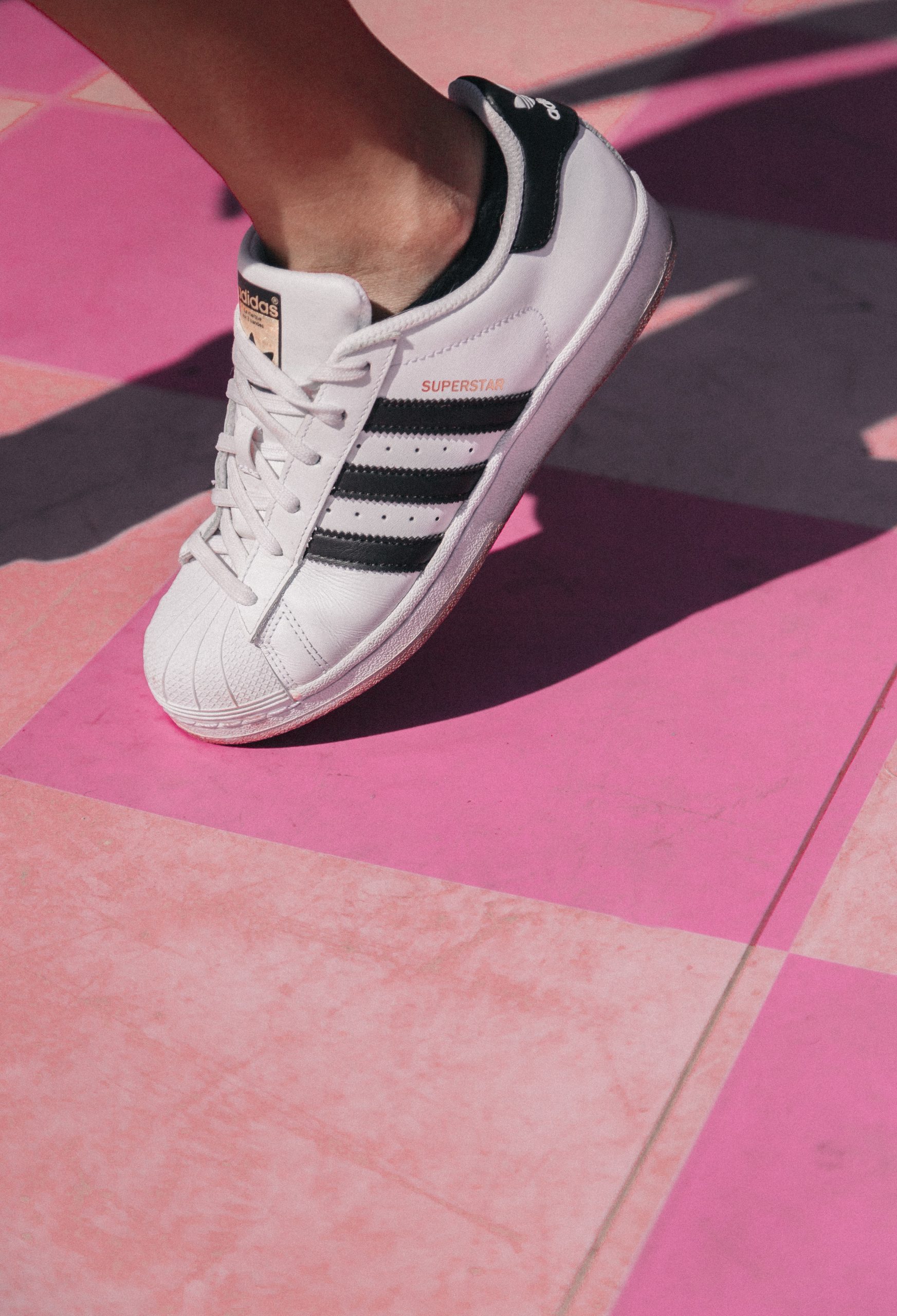 Person's foot, wearing Addidas Superstar shoes; white with black stripes.