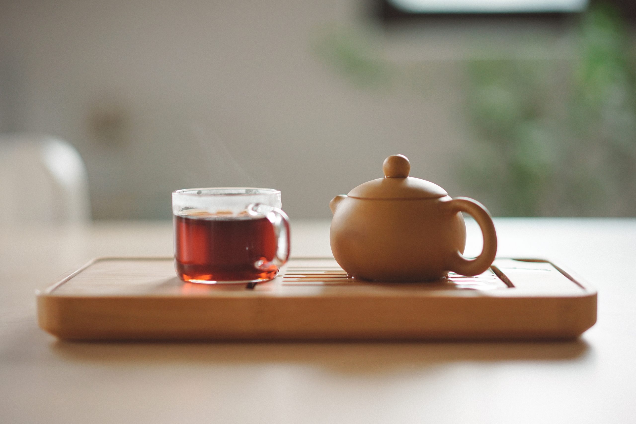Clear mug with tea next to a tea pot.