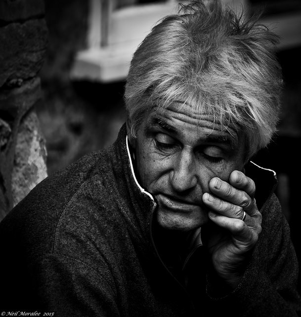 A dark, black and white photo of an older man looking downcast.