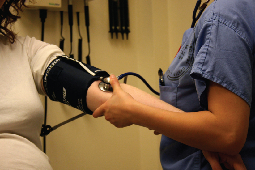 A person with a blood pressure cuff on their arm. A medical professional is taking their heart rate.