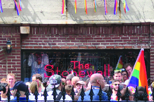 An image of a group of people standing in front of a brick building. A sign in the window of the building reads 