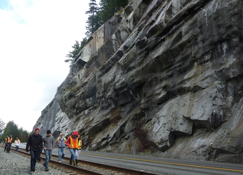 Figure 15.10 Site of the 2008 rock slide at Porteau Cove. Notice the prominent fracture set parallel to the surface of the slope. The slope has been stabilized with rock bolts (top) and holes have been drilled into the rock to improve drainage (one is visible in the lower right). Risk to passing vehicles from rock fall has been reduced by hanging mesh curtains (background). [SE photo 2012]