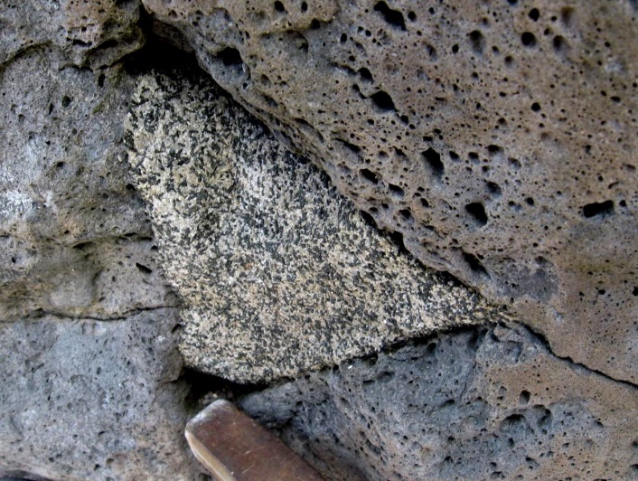 Figure 8.6a A xenolith of diorite incorporated into a basalt lava flow, Mauna Kea volcano, Hawaii. The lava flow took place some time after the diorite cooled, was uplifted, and then eroded. (Hammerhead for scale) [SE]