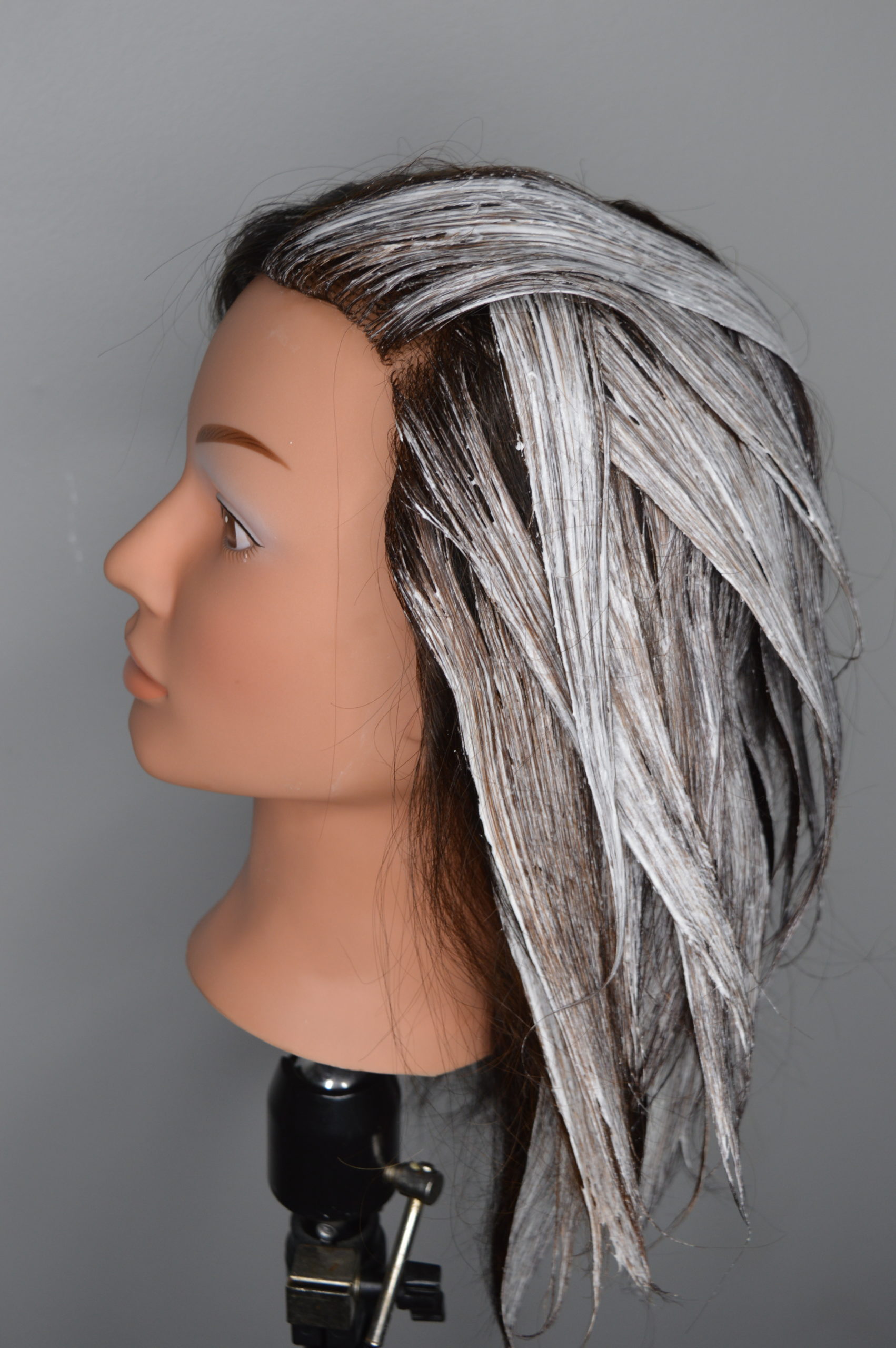 Lightener applied to strips of hair all over the head. Lightener is light near the roots and thinker near the ends.