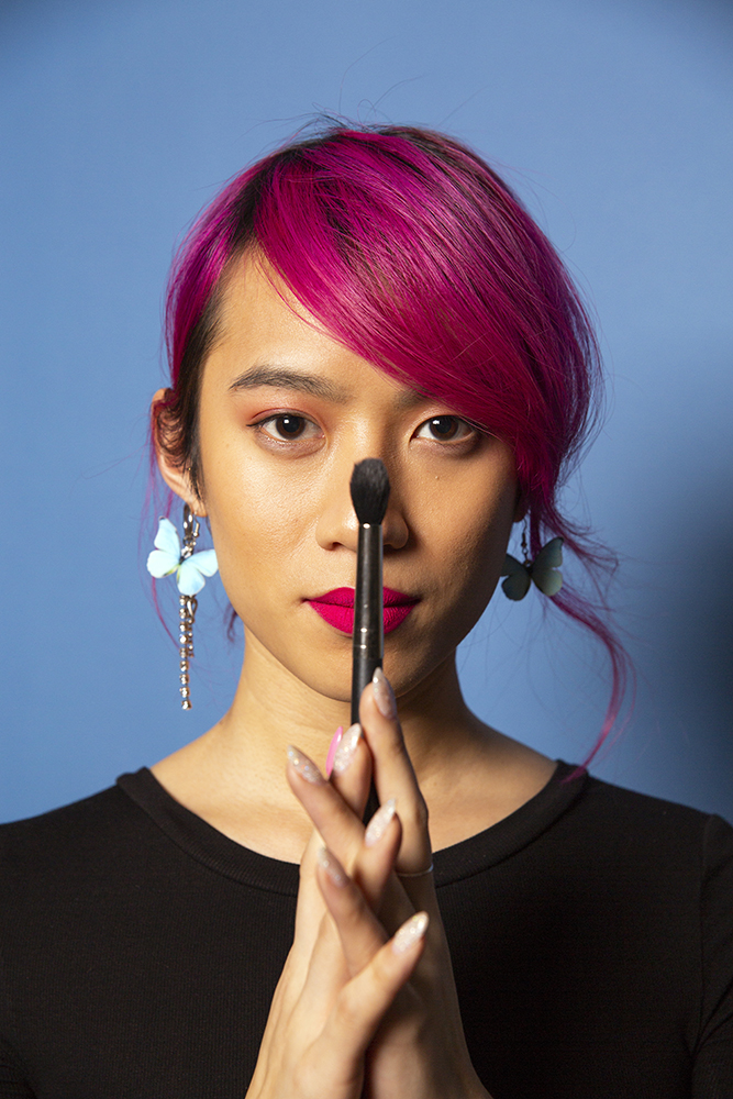 A non-binary femme using a makeup brush vertical