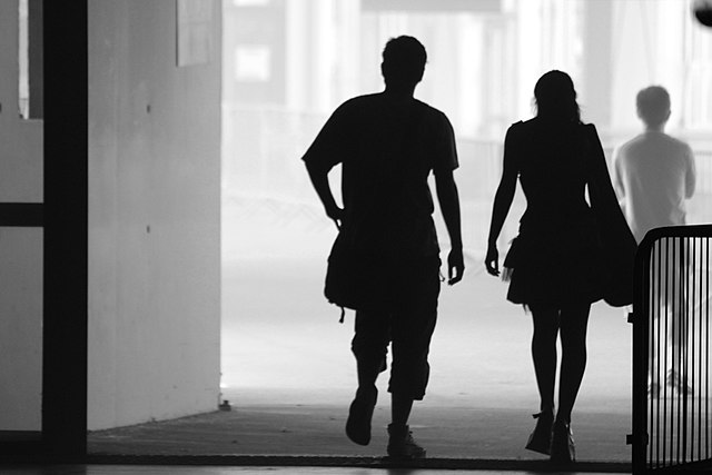 A man and woman are shown walking side by side through a concrete passage in silhouette.
