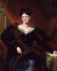 Painted portrait of a noble woman in a black gown and long brown fur stole sitting in a chair in front of a wine-coloured draped fabric. circa 1834
