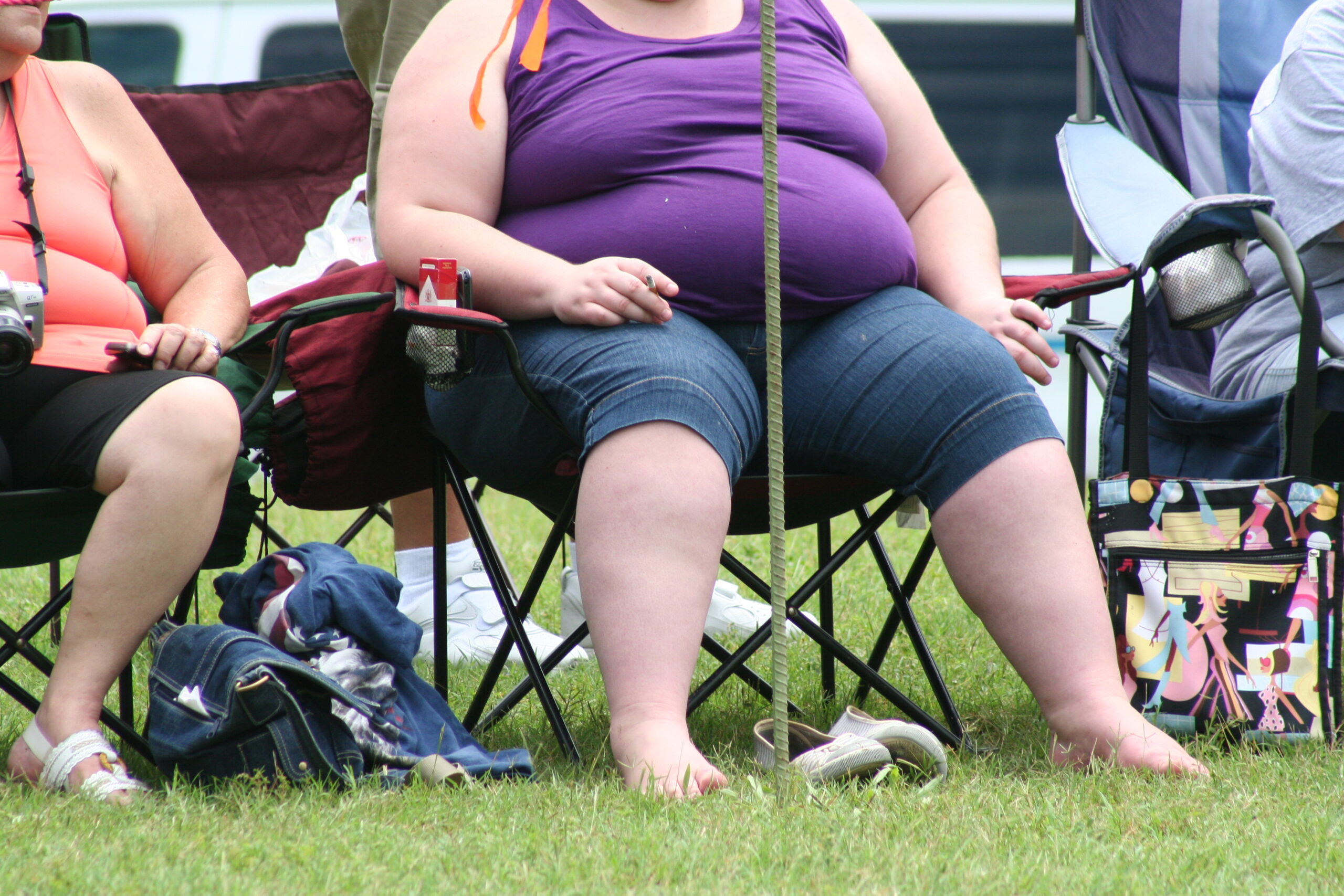 An overweight woman sitting in a chair, smoking.
