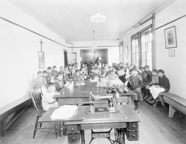Young aboriginal students sit on benches in a crowded classroom.