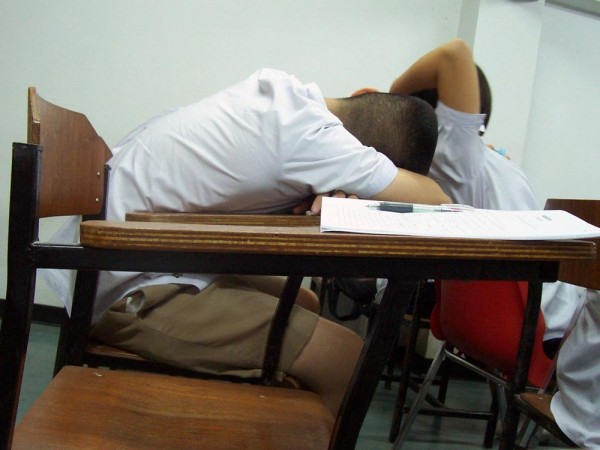 A boy with his head down sleeping on his school desk.