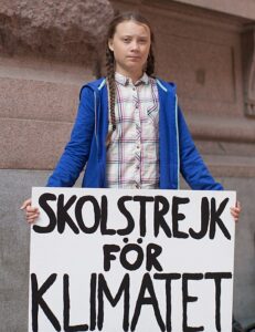 Greta Thunberg holding a sign that says School Strike for Climate in Swedish.