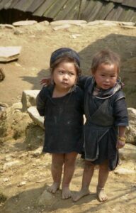 Two young Hmong girls in bare feet, one with arm around the other.