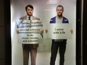 A Mac versus PC ad campaign. One man in an ill-fitting suit holds a sign ductaped together that says, "cobble, together, assorted software, to do music, movies and websites.'; The other man is dressed casually and holds a simple sign that says, "I come with iLife."