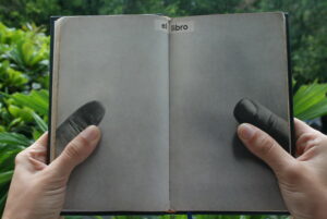 Picture of a book open to a page with photos of thumbs that appear to hold the book open. Below the thumb photos are the reader's actual thumbs.