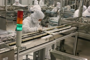 People working on an assembly line clothed in white suits that only leave the eyes uncovered.