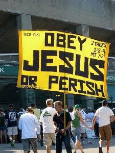 A man carries a large yellow sign that reads, "Obey Jesus or Perish."